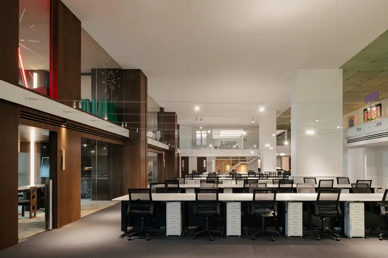 Open-plan office area with rows of workstations beneath a mezzanine and track lighting overhead