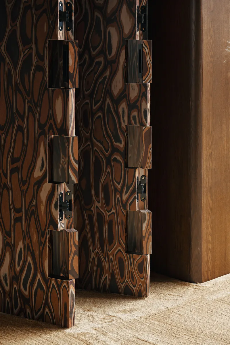 Figured wood door with custom black metal hinges and rectangular hardware against natural grain panels