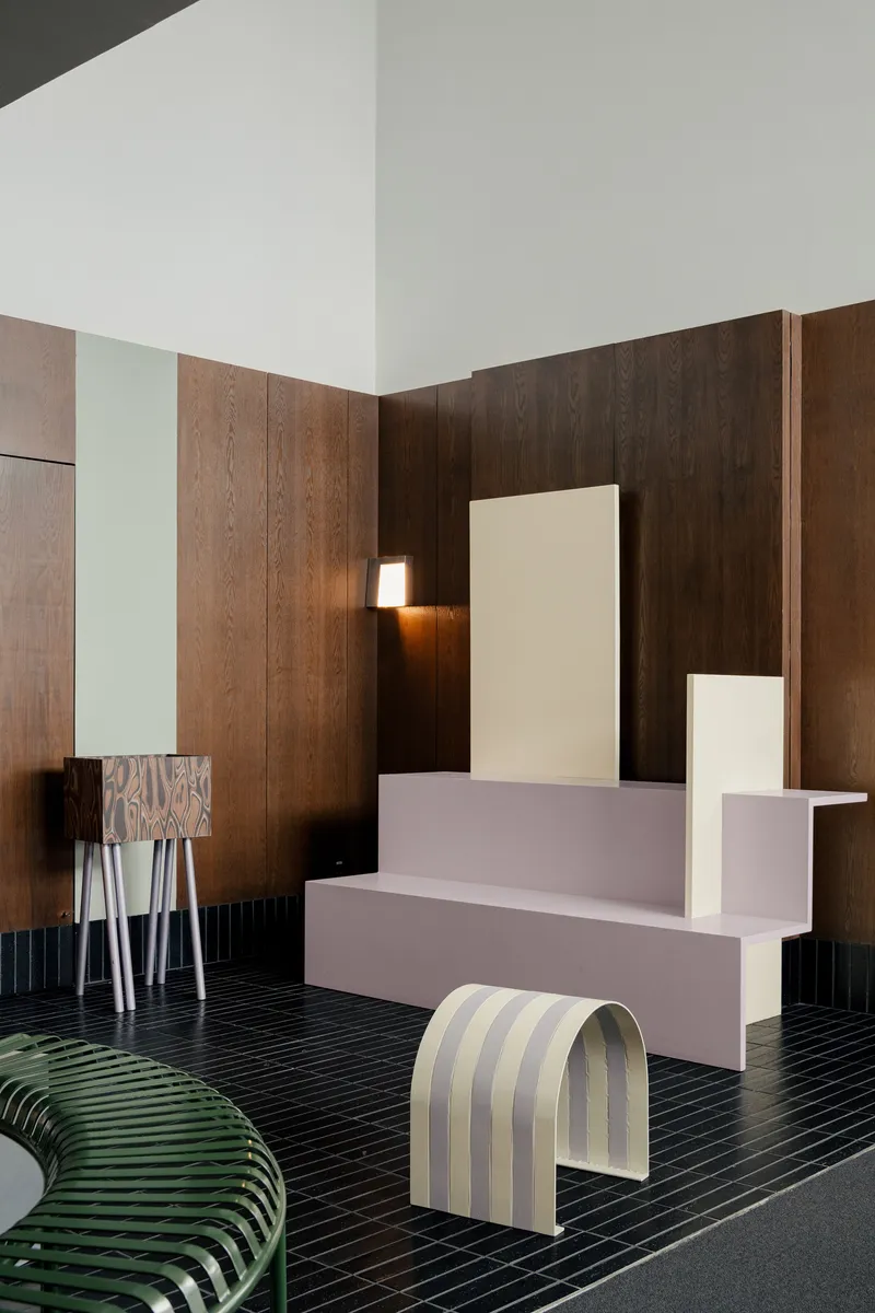 Reception desk in pale pink with timber wall paneling and striped upholstered seating on black tile floor