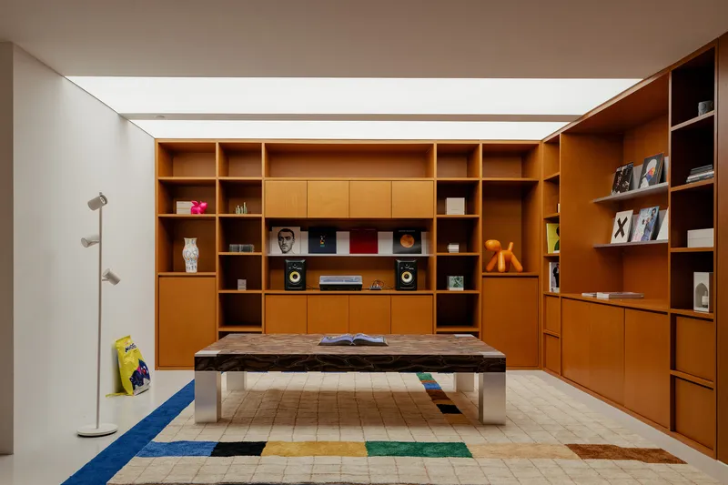 Floor-to-ceiling timber shelving unit with integrated display niches and cabinets under recessed ceiling cove lighting