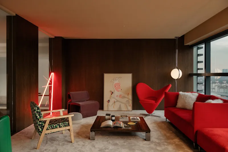 Living area with dark timber-paneled walls and red neon light sculpture beside upholstered seating