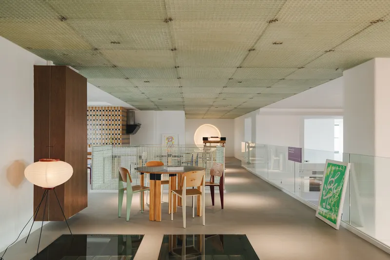 Double-height dining area with perforated acoustic ceiling panels and glass-railed mezzanine overlooking the space