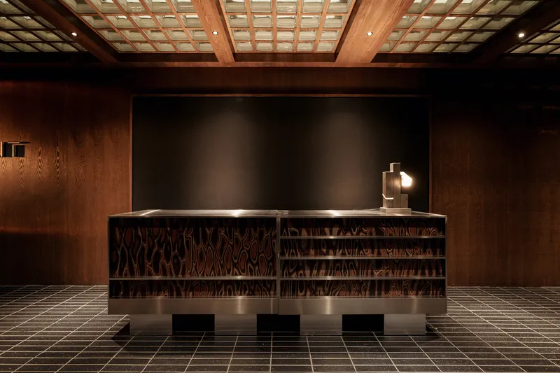 Reception desk with geometric patterned front panel below a timber coffered skylight ceiling and tiled floor