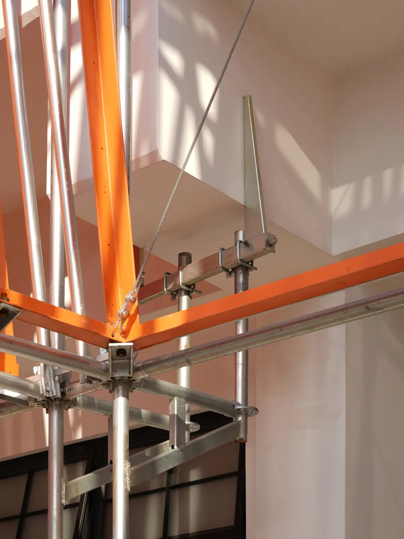 Detail of steel scaffolding joints connecting orange and silver tubular members with cable bracing