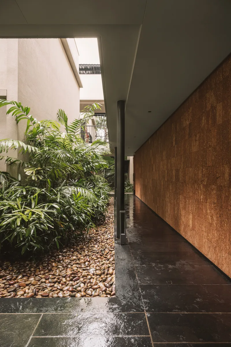 Covered passage with cork-clad walls alongside a planted courtyard with river pebbles and tropical plants