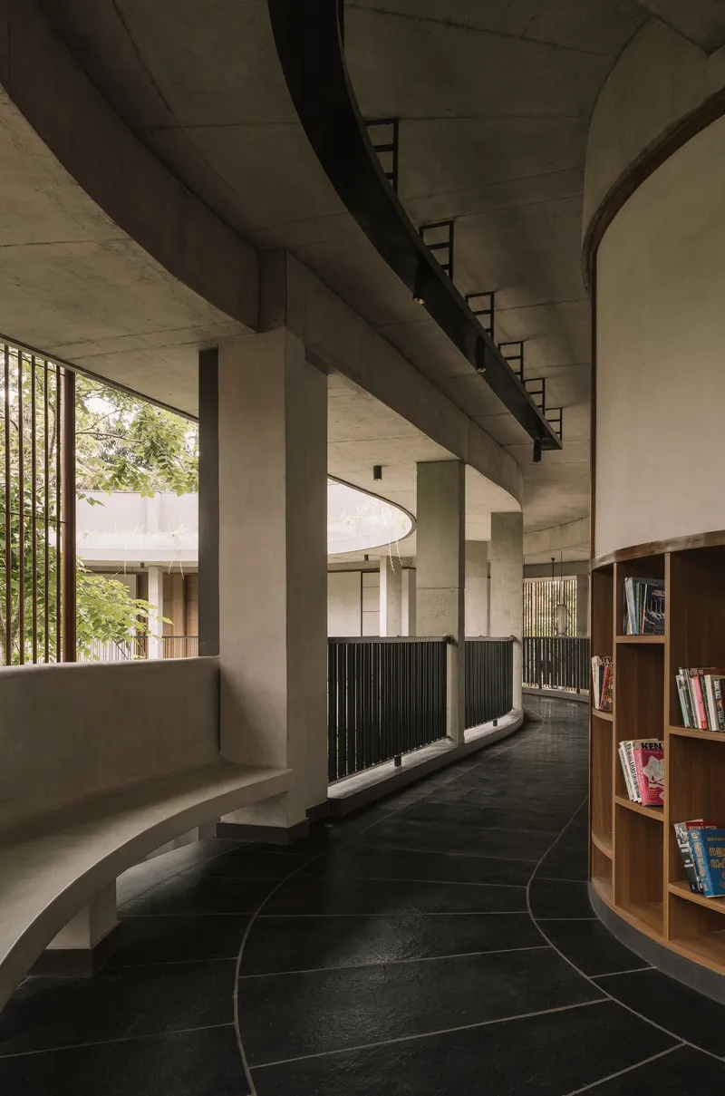 Interior corridor with exposed concrete ceiling beams and curved black tile floor alongside timber bookshelves