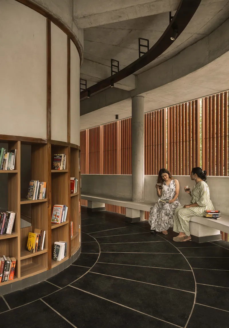 Library reading space with two seated figures beneath vertical timber louvers and concrete structural framework