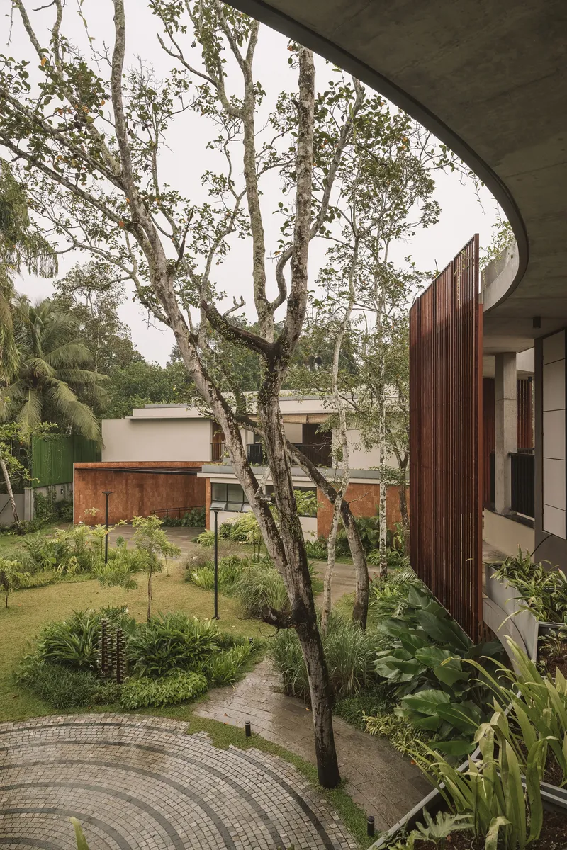 View from curved concrete balcony overlooking courtyard with mature trees and distant timber-clad volumes