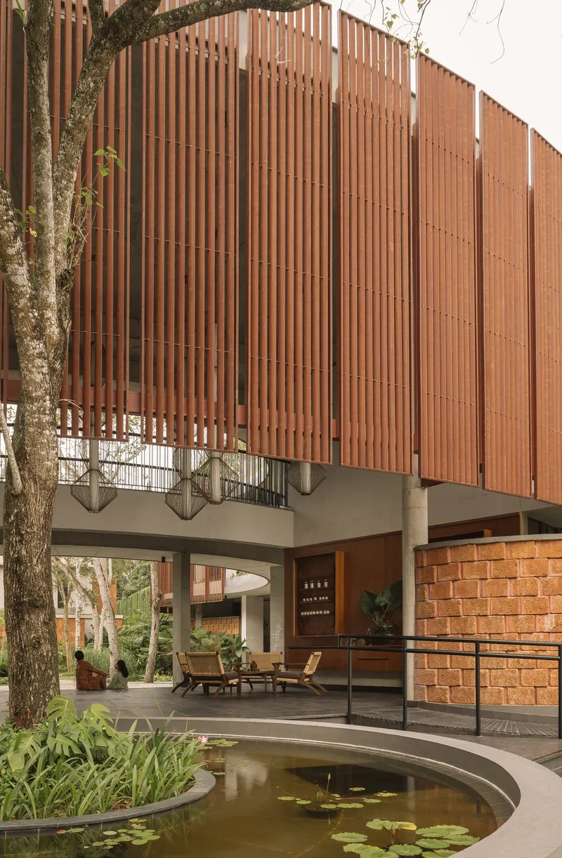 Curved reflecting pool beneath a raised volume with vertical timber louvers and concrete pilotis