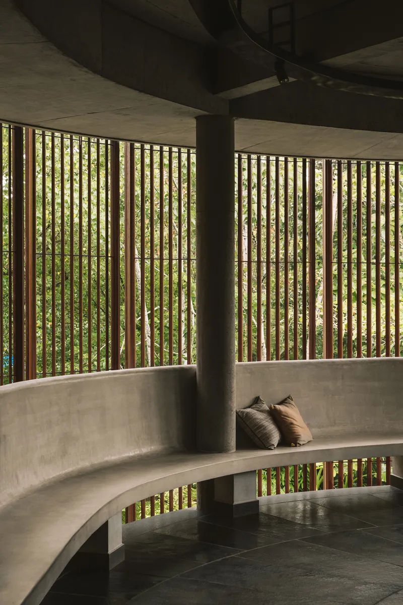 Curved concrete bench with timber screen filtering light into a shaded interior seating area