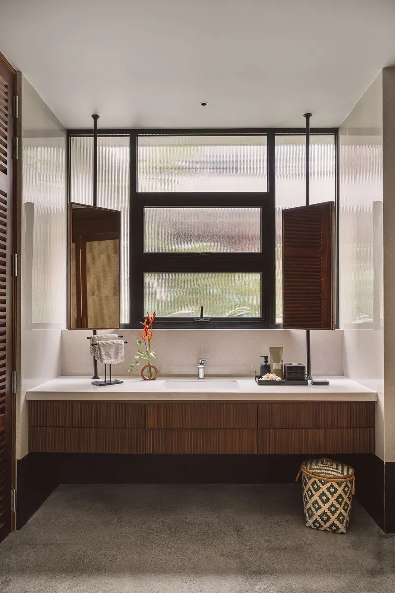Bathroom vanity with timber cabinetry beneath a window with fluted glass and operable louvered shutters