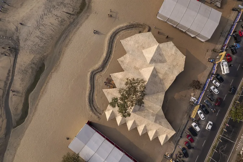 Aerial view of the zigzag woven roof surrounding a tree in a sandy compound