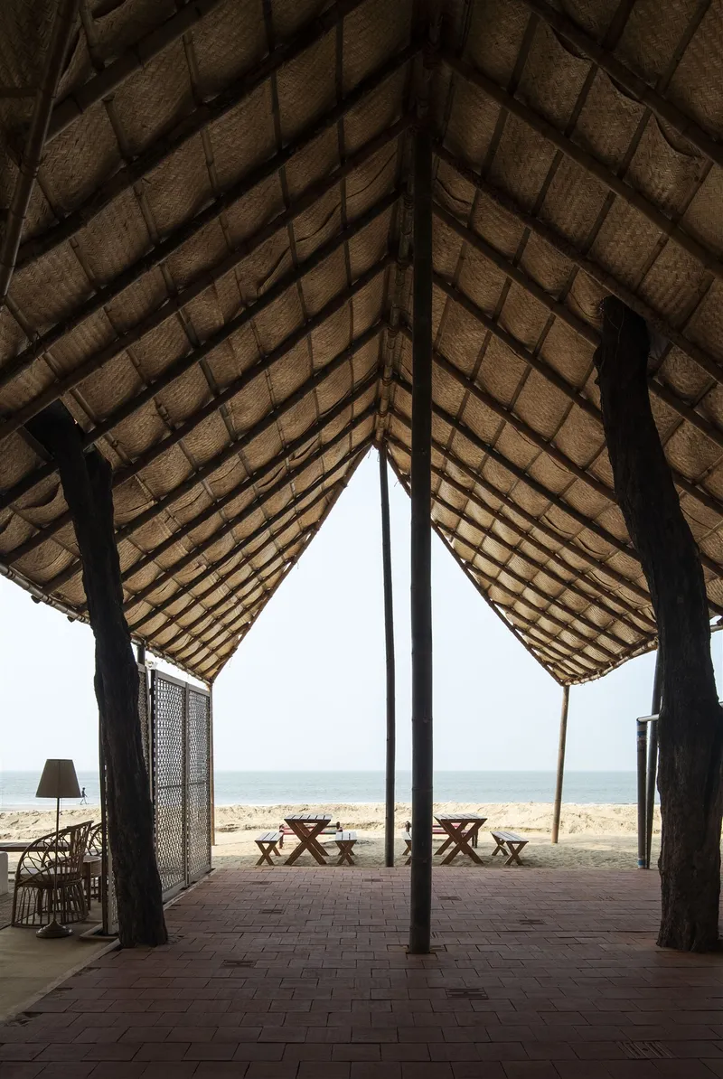 Interior view through a thatched pavilion with timber columns framing the ocean beyond