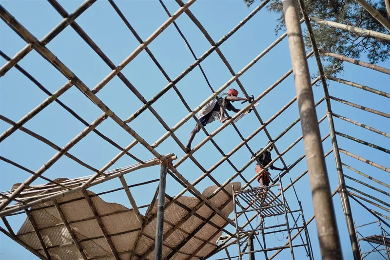 Worker assembling bamboo lattice framework for a roof structure under clear sky