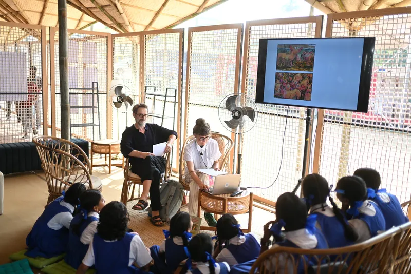 Interior classroom space with bamboo lattice walls and schoolchildren seated on the floor