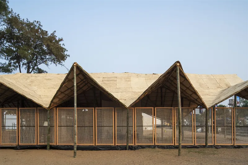 Timber post and mesh panel facade beneath the undulating woven roof in daylight