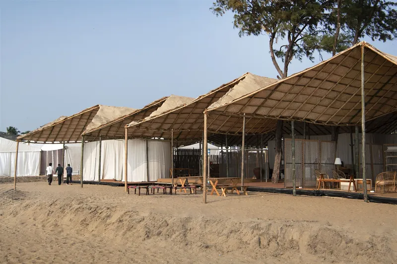 Side elevation showing fabric curtains and timber benches on sand below repeating peaked roof forms