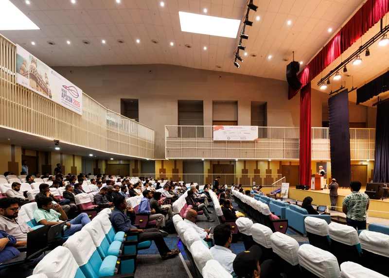 Interior view of the auditorium showing wood-paneled balconies and ceiling lit by recessed spotlights during an assembly