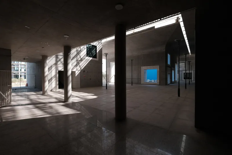 Interior ground floor with polished concrete columns casting diagonal shadows across the floor from clerestory light above