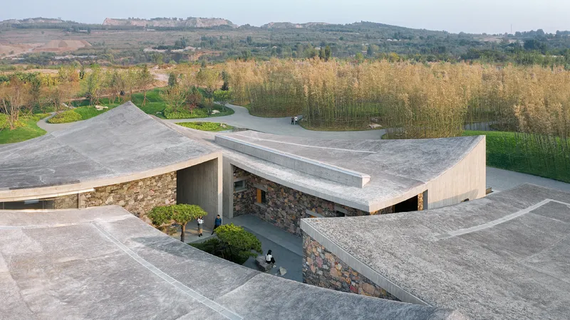 Aerial view of angular concrete roof planes punctured by a courtyard over stone masonry walls in autumn