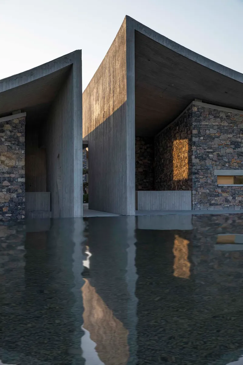 Covered entry passage with board-formed concrete columns and shallow reflecting pool catching late afternoon light