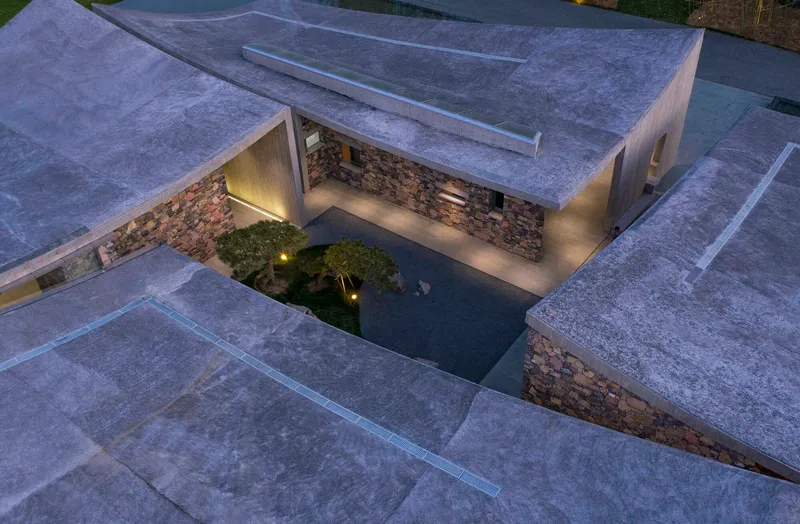 Drone view at dusk showing the illuminated stone-walled courtyard carved into concrete roof planes
