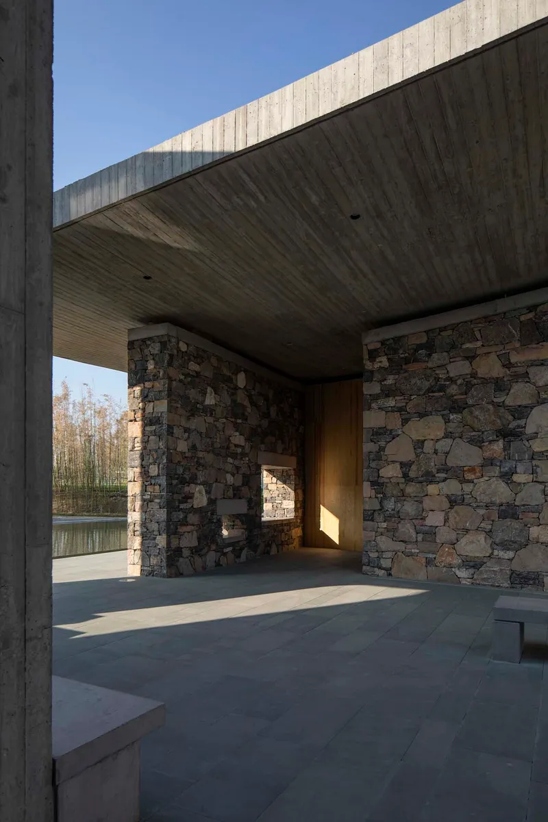 Covered terrace with board-formed concrete soffit and fieldstone walls opening to a reflecting pool