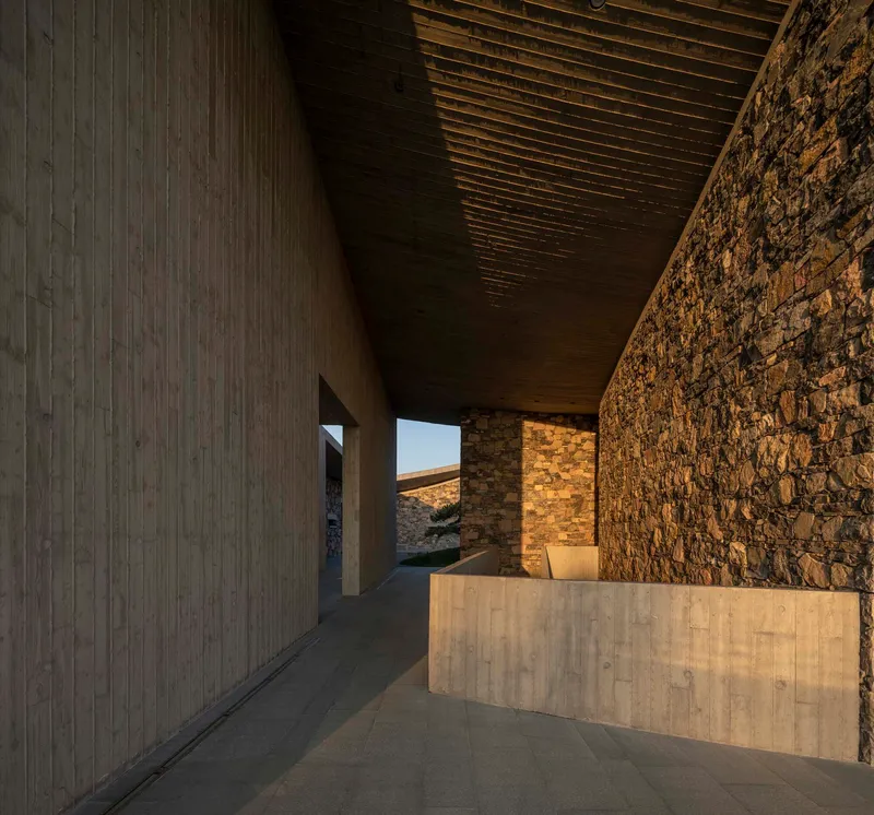Interior corridor at dusk with exposed timber ceiling joists between concrete and stone walls
