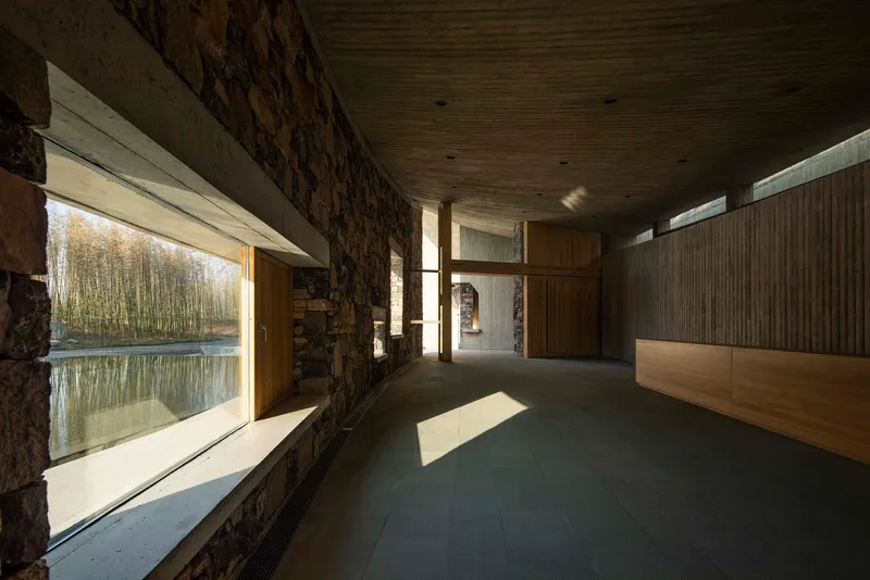 Corridor with stone wall and horizontal window overlooking a pond and birch trees in autumn