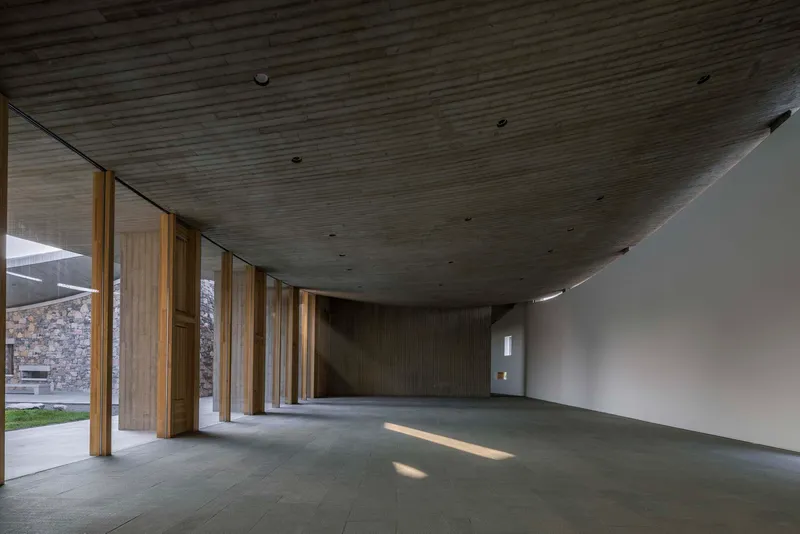 Gallery space with angled timber ceiling and timber columns opening to a courtyard