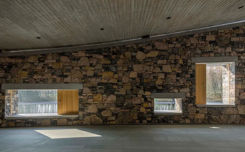 Fieldstone wall with timber-framed windows and clerestory slot admitting afternoon sunlight
