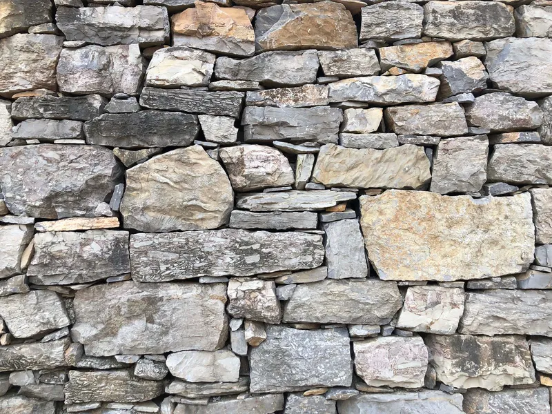 Dry-stacked fieldstone wall in grey and tan tones with varied coursing and natural patina