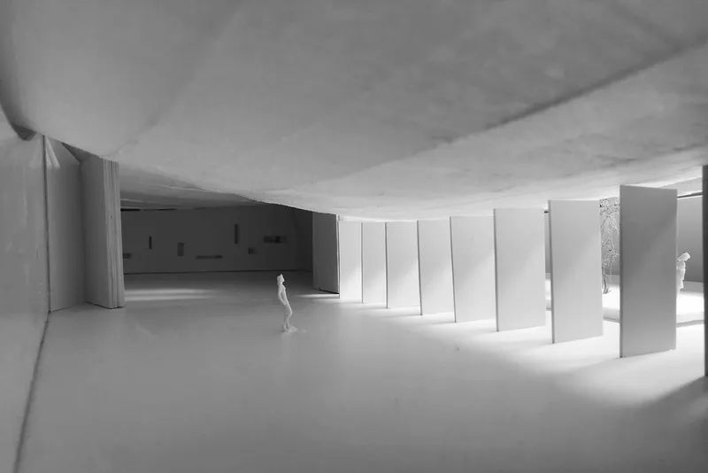 Physical model interior with a figure walking through curving gallery space lit by vertical slots