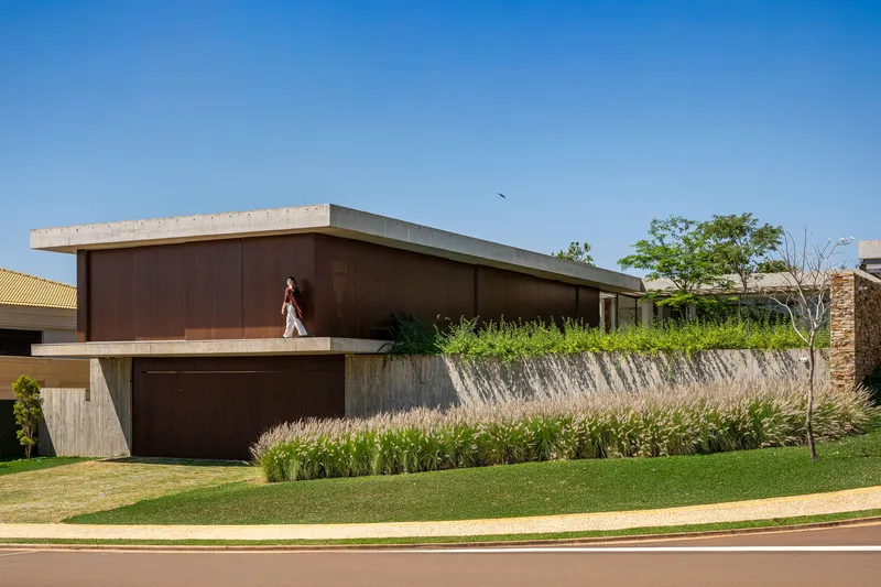 Street view of the dark timber-clad upper volume with concrete soffit above planted grasses and lawn