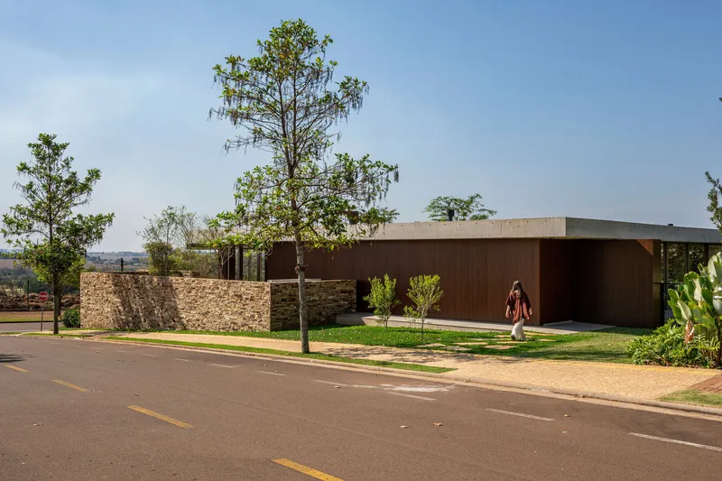 Stone perimeter wall and dark timber facade from the street with scattered trees under clear sky