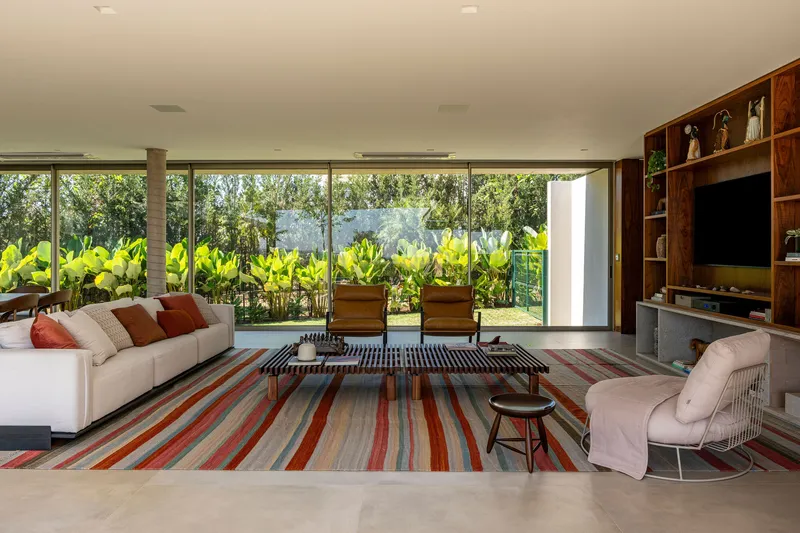 Living room with striped rug and floor-to-ceiling glazing opening to a terrace with banana plants