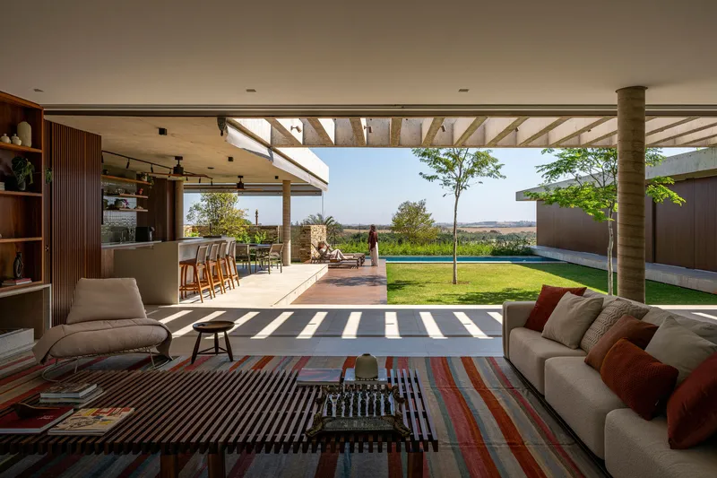 Interior view through the open living pavilion toward the lawn and distant landscape under timber beams