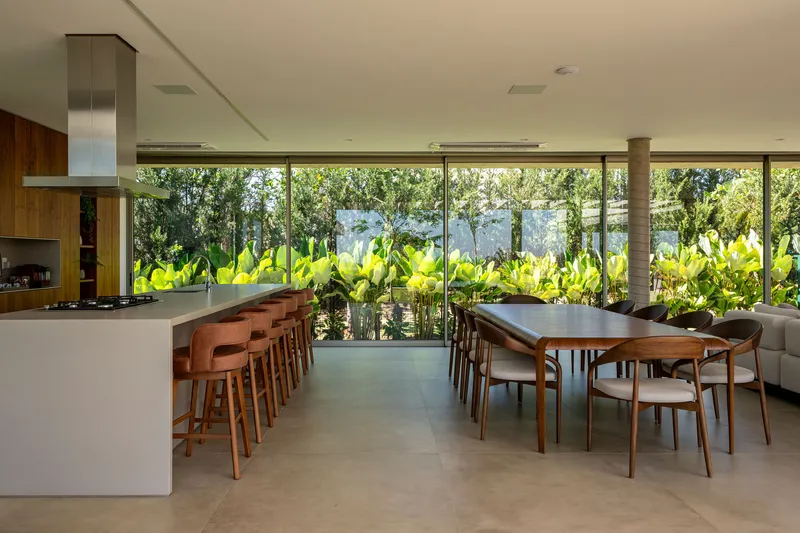 Dining area with kitchen island and glass wall overlooking planted bed of large-leafed tropical vegetation