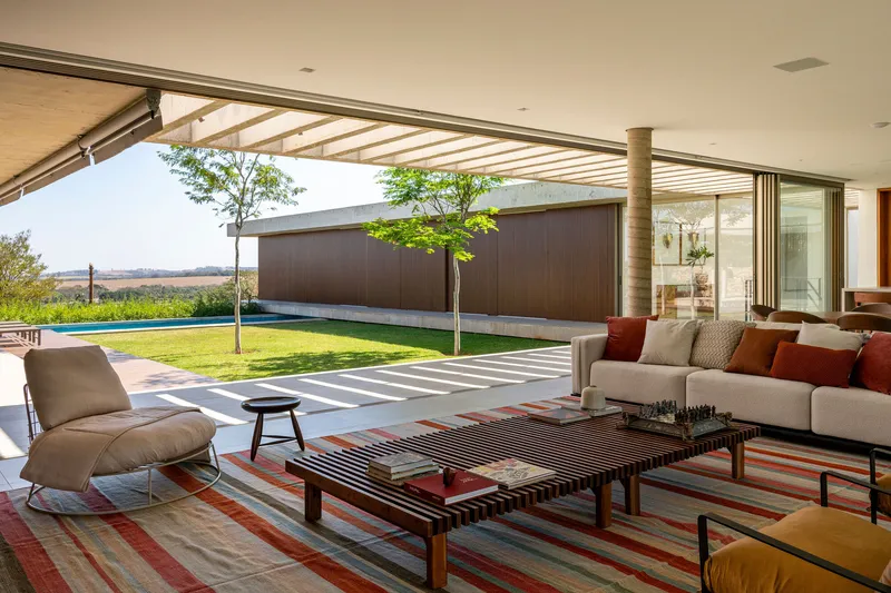 Living room opening to courtyard with pool and grass lawn under a slatted canopy