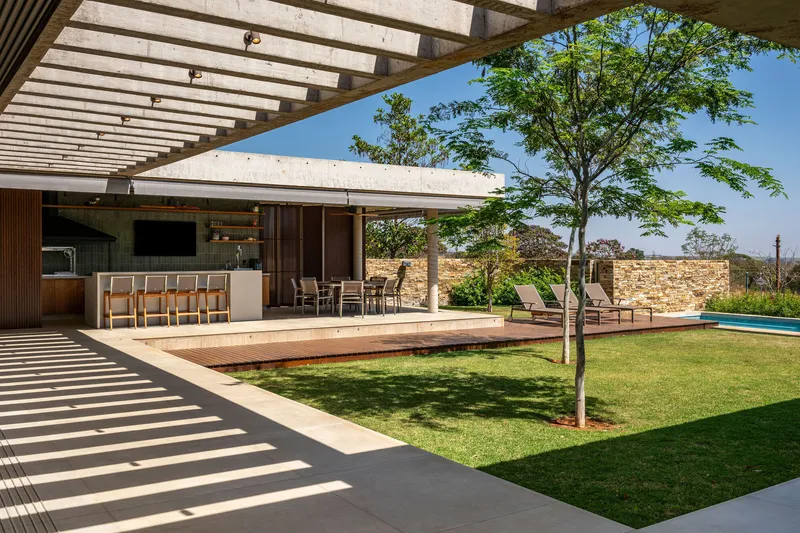 Covered terrace with concrete pergola beams casting shadows onto the lawn and outdoor kitchen