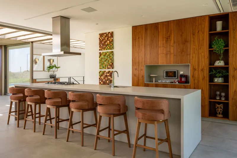 Kitchen island with leather upholstered stools facing a timber wall with integrated appliances