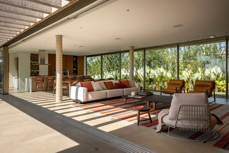 Open living space with concrete columns and floor-to-ceiling glass overlooking planted garden beds