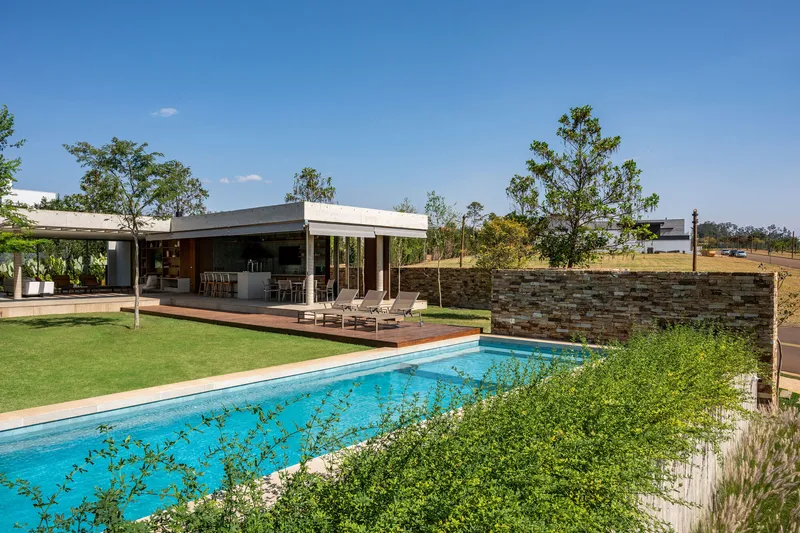 Lap pool edged with planted beds and a stone wall under a clear afternoon sky