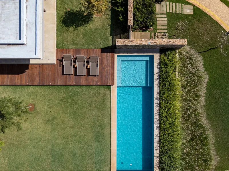 Aerial view of the lap pool bordered by timber decking and three lounge chairs in green lawn