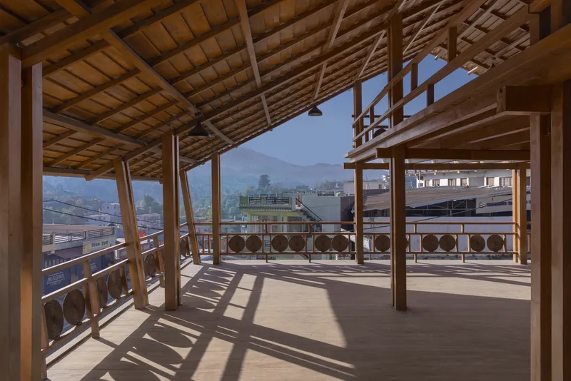 Interior of timber-framed pavilion with column shadows across the floor and mountain vista through open sides