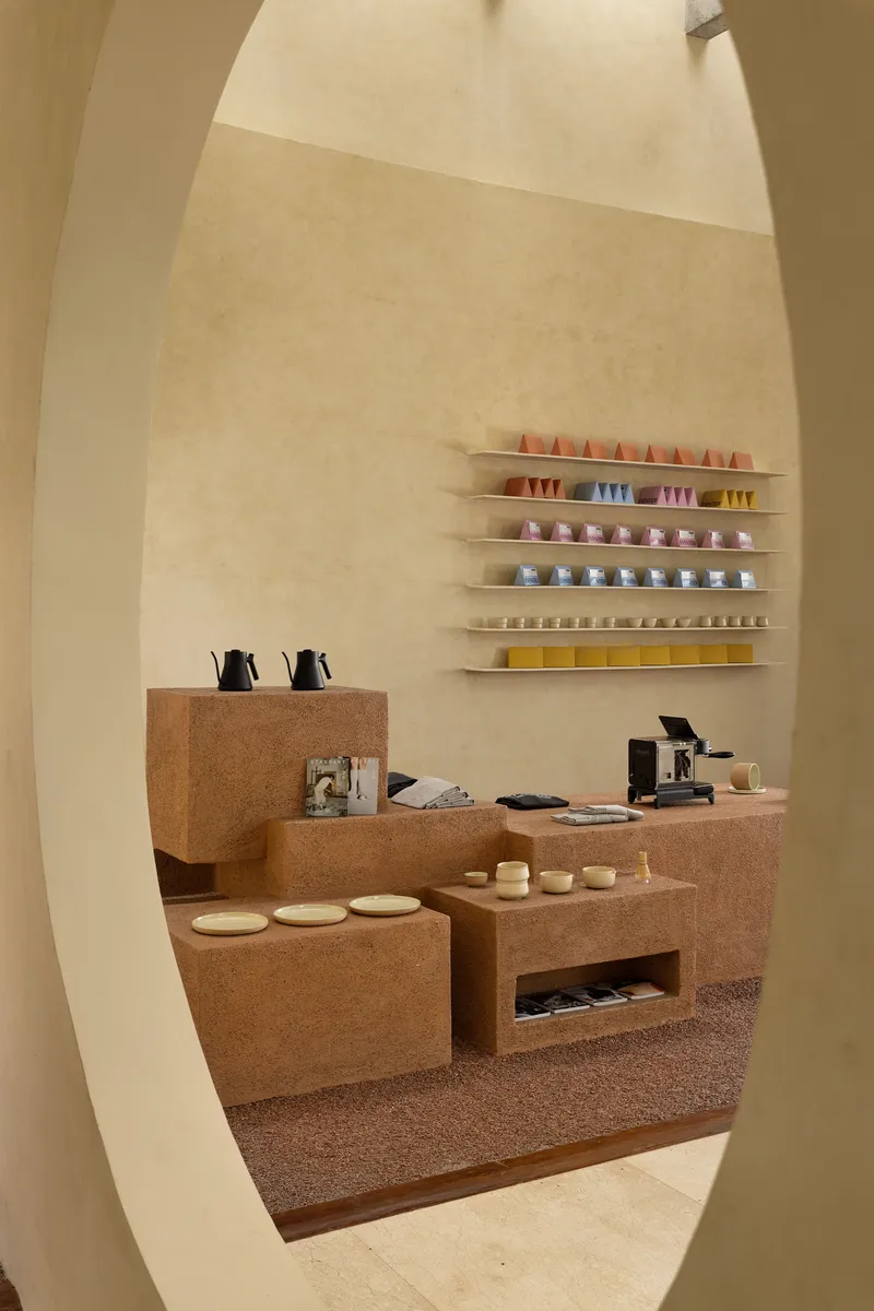 View through curved opening to coffee counter with cork surfaces and colorful cups on wall shelves