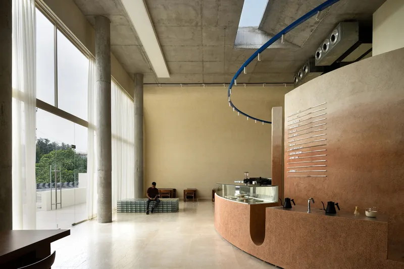 Double-height cafe interior with floor-to-ceiling windows and person seated near the curved cork counter