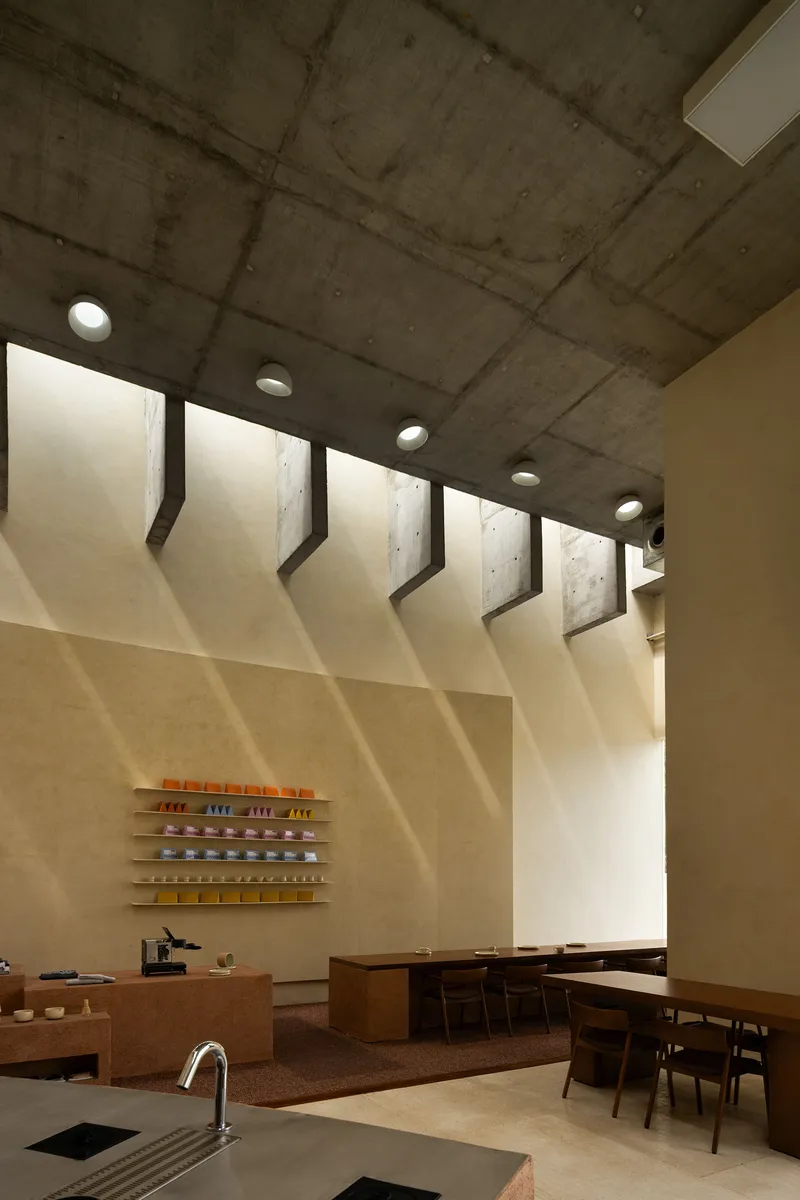 Sawtooth skylight profile casting diagonal shadows across plaster wall and seating area