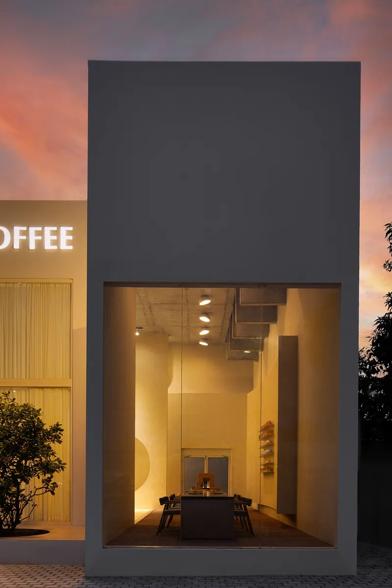 Tall glazed opening framing an illuminated staircase and table at dusk with pink sky