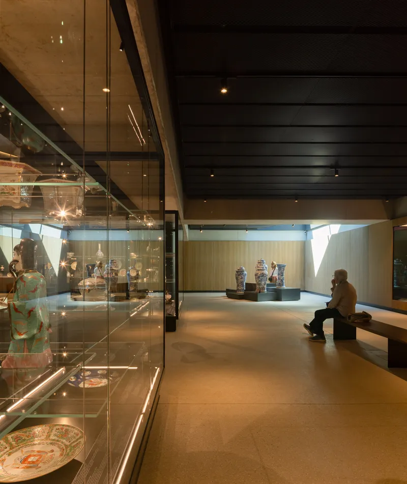 Gallery interior with glass display cases and seated visitor beneath black ceiling and timber wall